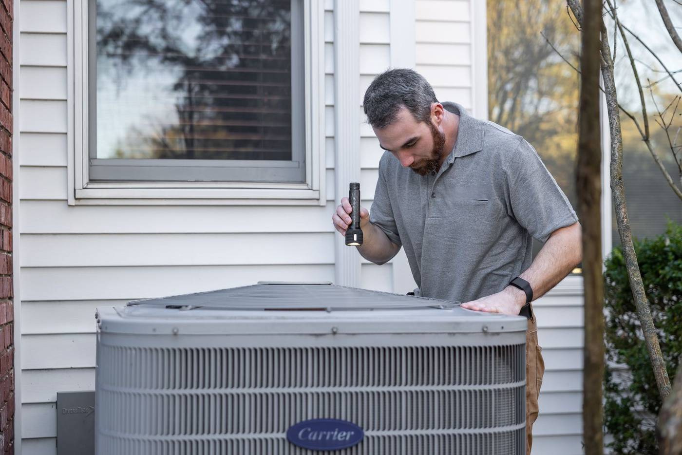 Technician inspecting an outdoor air conditioning unit with a flashlight