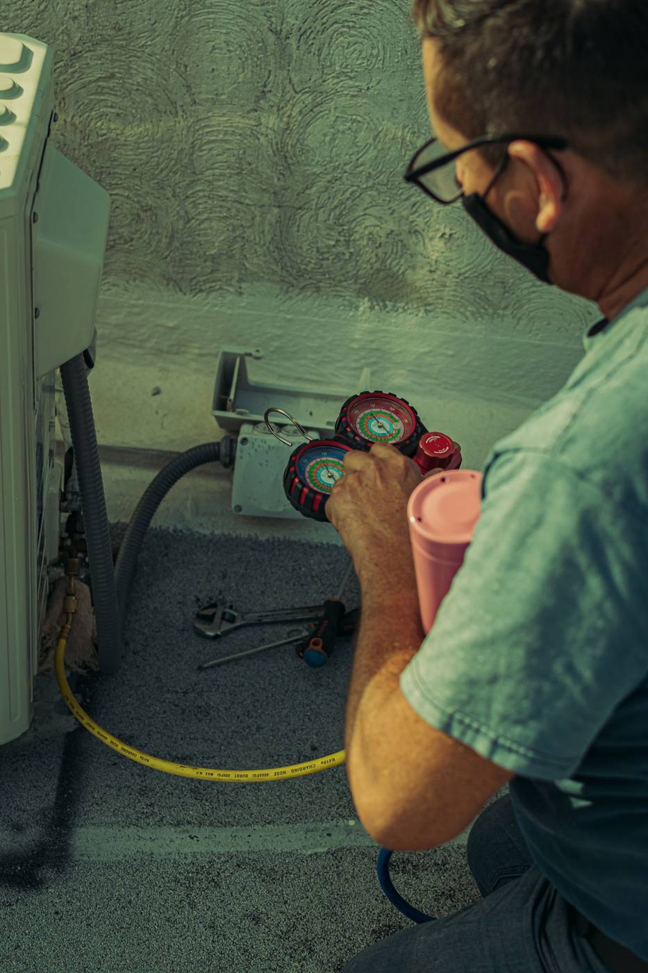 Technician with manifold gauges servicing an outdoor unit